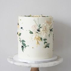 a white cake with flowers on it sitting on top of a wooden stand next to a wall