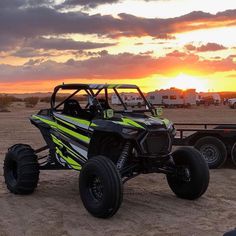 a yellow and black buggy is parked in the sand near some trucks at sunset