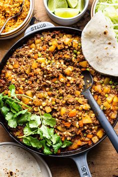 a skillet filled with taco meat and vegetables next to tortilla shells