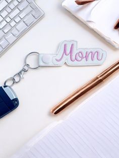 a keychain with the word mom on it sitting next to a computer keyboard