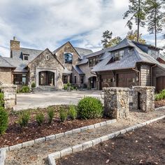 a large house with stone walls and lots of trees in the front yard, surrounded by landscaping