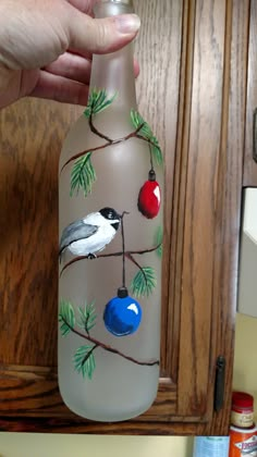 a hand is holding a painted glass bottle in the shape of a bird on a tree branch