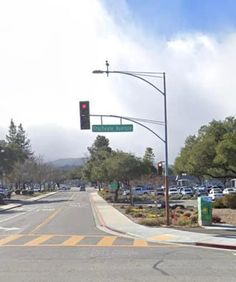 an empty street with cars parked on the side and traffic lights hanging over the road