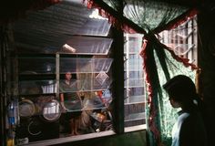 two people standing in front of a window with curtains on it and some dishes hanging from the ceiling