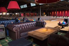 a bowling alley with leather couches, tables and lights hanging from the ceiling above