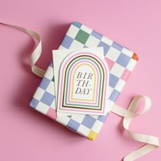 a birthday card sitting on top of a pink surface next to a ribbon and paper