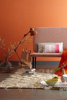 a living room with an orange wall and white rugs on the floor next to a pink couch