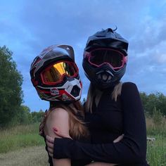 two people with helmets on their heads hugging each other in the middle of a field