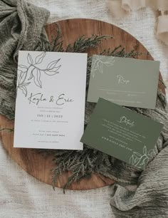 the wedding stationery is laid out on a wooden platter with greenery and foliage