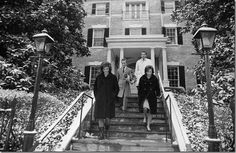 three people are standing on the stairs in front of a building with trees and bushes