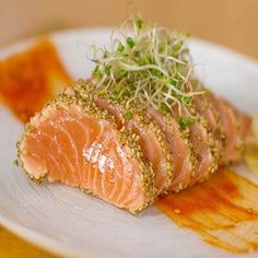 a white plate topped with salmon covered in sauce and sprouts on top of it