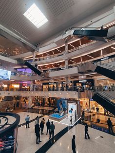 people are walking around in an indoor shopping mall with escalators and staircases