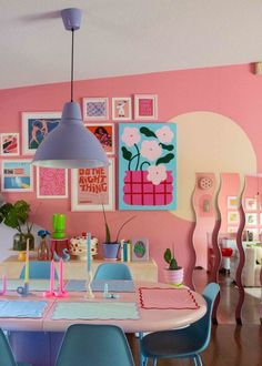 a dining room with pink walls and pictures on the wall, blue chairs and table