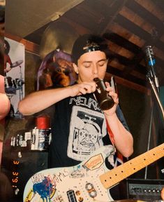 a man holding a guitar and drinking from a bottle while standing in front of a microphone