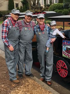 three men in overalls and hats standing next to a small train