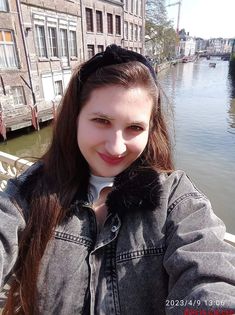 a woman taking a selfie in front of some buildings on the riverbank with her hands behind her head