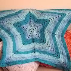 a blue crocheted blanket sitting on top of a white couch next to an orange pillow