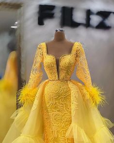 Elevate your evening look with this stunning yellow lace gown, designed to make a bold statement. The intricate embroidery on the body adds an element of sophistication, while the deep V-neck and fitted silhouette enhances your natural curves, exuding elegance and confidence. Ideal for gala events, weddings, or any grand occasion, this gown ensures all eyes will be on you.The distinct long sleeves feature delicate feather accents at the cuffs, infusing whimsical charm into the overall design. La Corn Wedding, Ankara Tops, African Traditional Wedding, Lace Evening Gowns, Gala Events, Yellow Lace, Intricate Embroidery, Natural Curves, Tulle Fabric