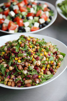 two plates filled with salad on top of a metal table next to bowls of vegetables