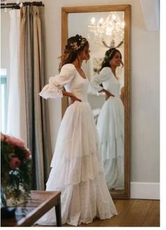 a woman standing in front of a mirror wearing a white wedding dress with ruffles