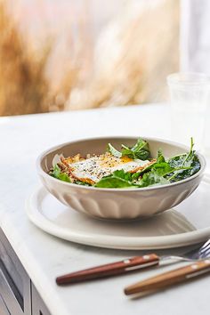 a white plate topped with a salad next to a glass of water and utensils