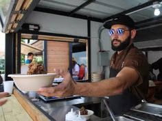 a man holding a bowl with food in it while standing next to a counter top