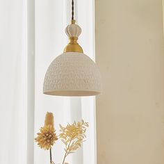 a white lamp hanging from a ceiling next to a vase with flowers