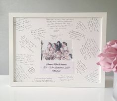 a vase filled with pink flowers sitting next to a white framed photo on top of a table