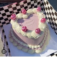 a heart shaped cake with cherries on top in a checkerboard pattern box