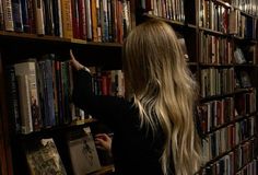 a woman is pointing at books on a book shelf in a library full of books