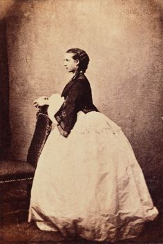 an old photo of a woman in a long white dress with a fan on her lap