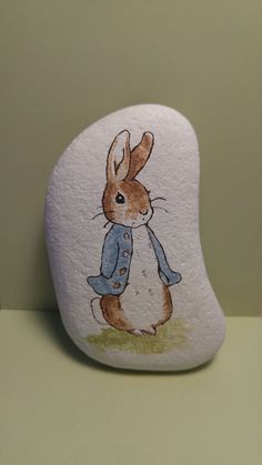 a rock with a painting of a rabbit wearing a blue jacket on it's face