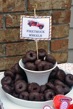 there is a white bowl full of chocolate donuts on the table with a sign that says firetruck wheels