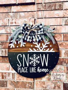 a snow place like home sign hanging on the side of a brick building with a bow