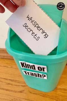 a hand holding a piece of paper over a green trash can