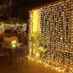 a patio covered in fairy lights and decorated with flowers on the outside wall, next to an outdoor dining table