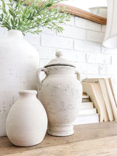 two white vases sitting on top of a wooden table next to a book shelf