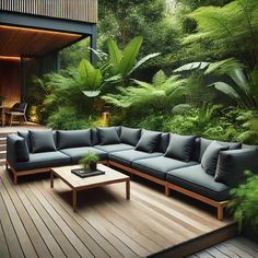 a couch and table on a wooden deck in front of a house surrounded by greenery