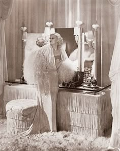 an old fashion photo of a woman standing in front of a mirror with feathers on it