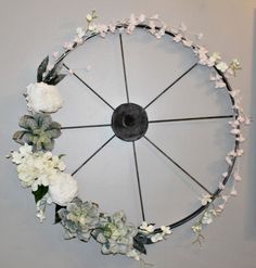 a wheel decorated with flowers and greenery hangs on the wall in front of a gray wall