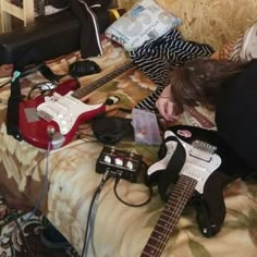 a woman laying on top of a bed next to two electric guitars and an amp