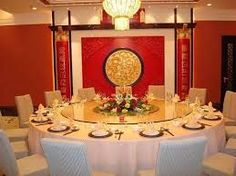 a large round table with white chairs and plates on it in front of a red wall