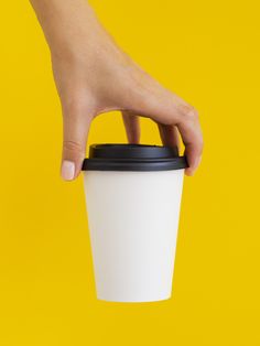 a hand holding a coffee cup over a yellow background