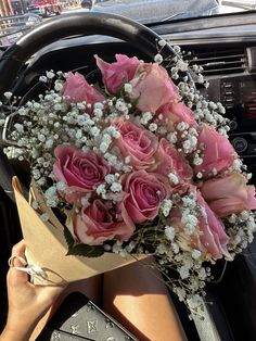 a bouquet of pink roses sits in the drivers seat of a car as she holds onto her steering wheel