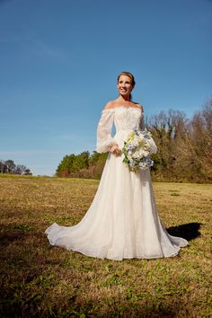 a woman in a wedding dress standing on the grass with her arms around her waist