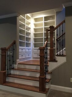 an empty room with wooden stairs and white shelving units on the wall behind them