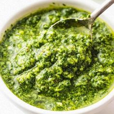 a white bowl filled with pesto sauce and a spoon in the bowl next to it