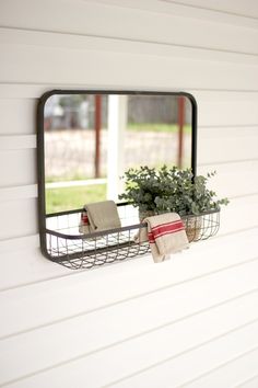 a mirror mounted to the side of a white wall next to a potted plant