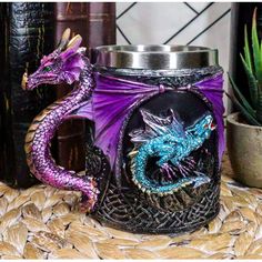 a purple and blue dragon mug sitting on top of a table next to a potted plant