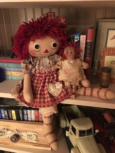 a doll is sitting on a shelf next to other dolls and books in a bookcase